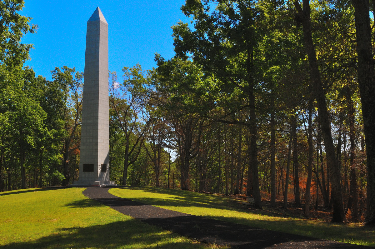 The U.S. Monument at Kings Mountain National Military Park, a tall stone obelisk rising from a grassy hill surrounded by forest, commemorating the Revolutionary War battle site.