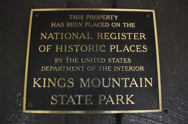 A bronze plaque mounted on dark wood at Kings Mountain State Park, stating that the property has been placed on the National Register of Historic Places by the United States Department of the Interior. The plaque reflects the park’s recognized historical importance and preservation as part of America’s heritage.